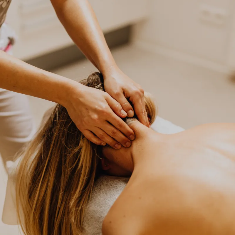 A massage therapist's hands gently massaging a person's neck and head.